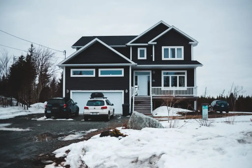 Snow-covered house with cars parked outside garage in winter